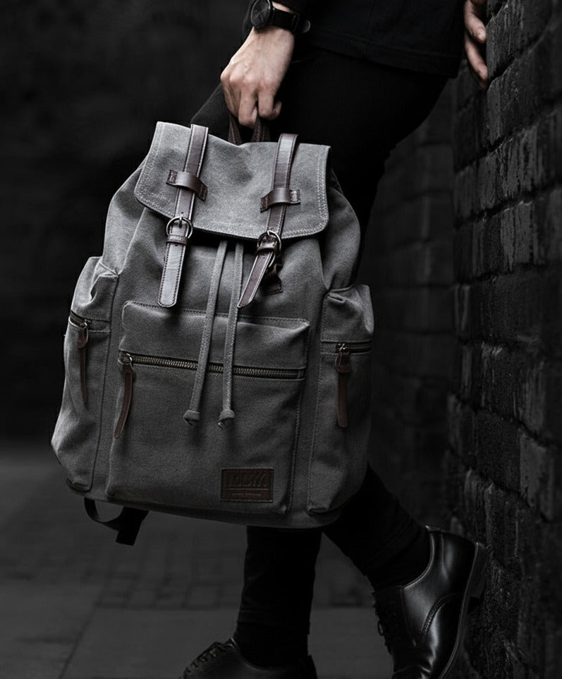 Person holding a gray backpack against a brick wall.